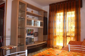 A room with a bed, a television, a cabinet with glass doors, and a window with curtains.