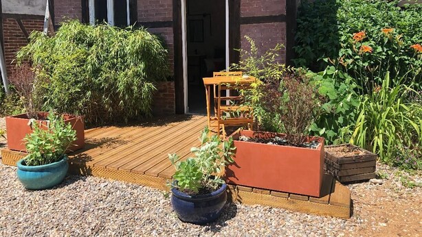Une terrasse en bois agrémentée de plantes en pot et d’un banc en bois.