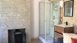 Une pièce avec un mur en pierre, une douche en verre, un meuble en bois et un canapé agrémenté d’un coussin à motifs.