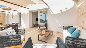Ein moderner, offener Wohnbereich mit Sofa, Sesseln und Couchtisch. Ein großes Fenster bietet Blick auf das Meer.