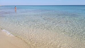 Ein Strand mit klarem, seichten Wasser und einer Person in der Ferne.