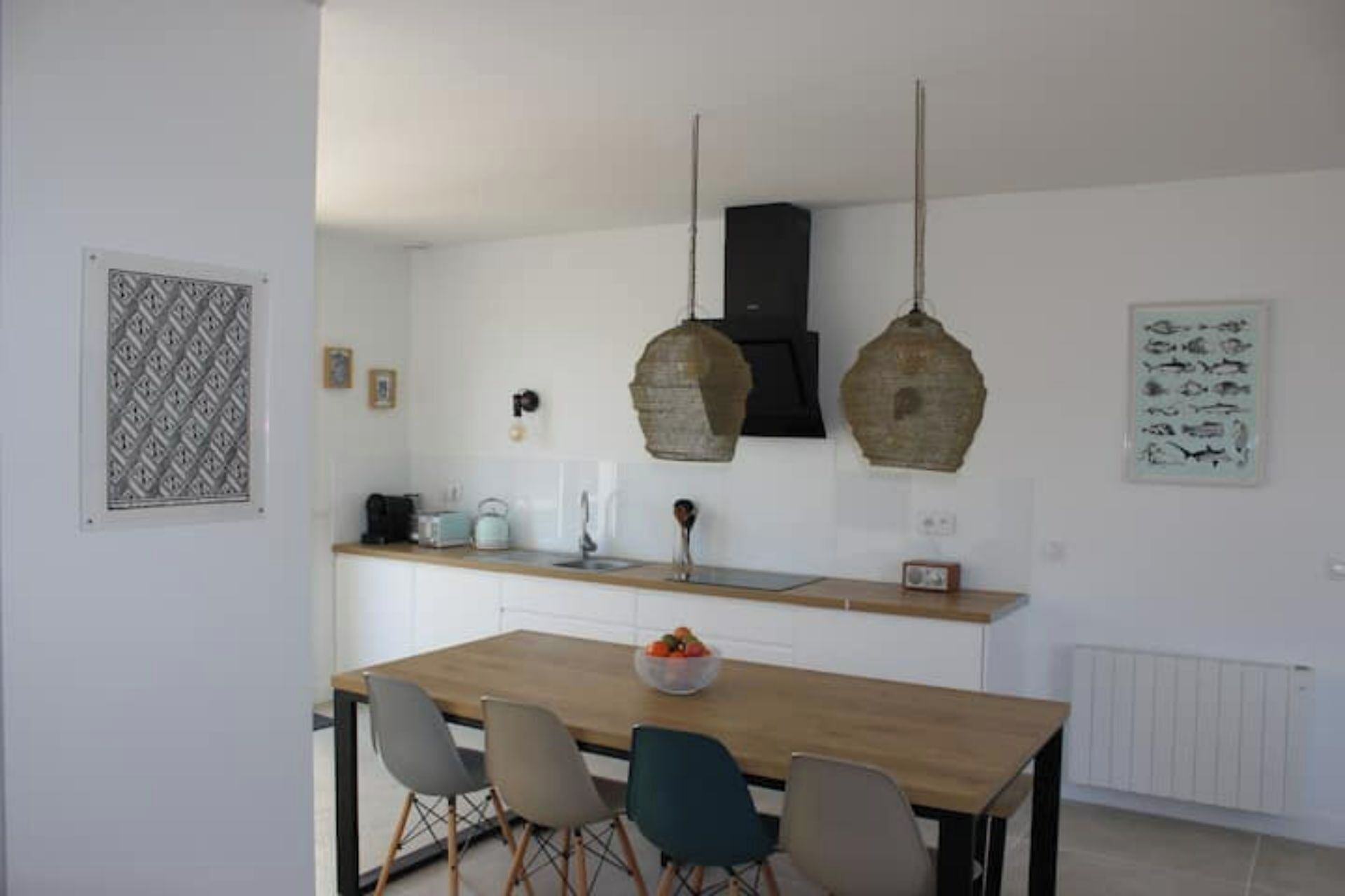 Une cuisine moderne avec une table à manger en bois, deux luminaires suspendus et un revêtement mural blanc.
