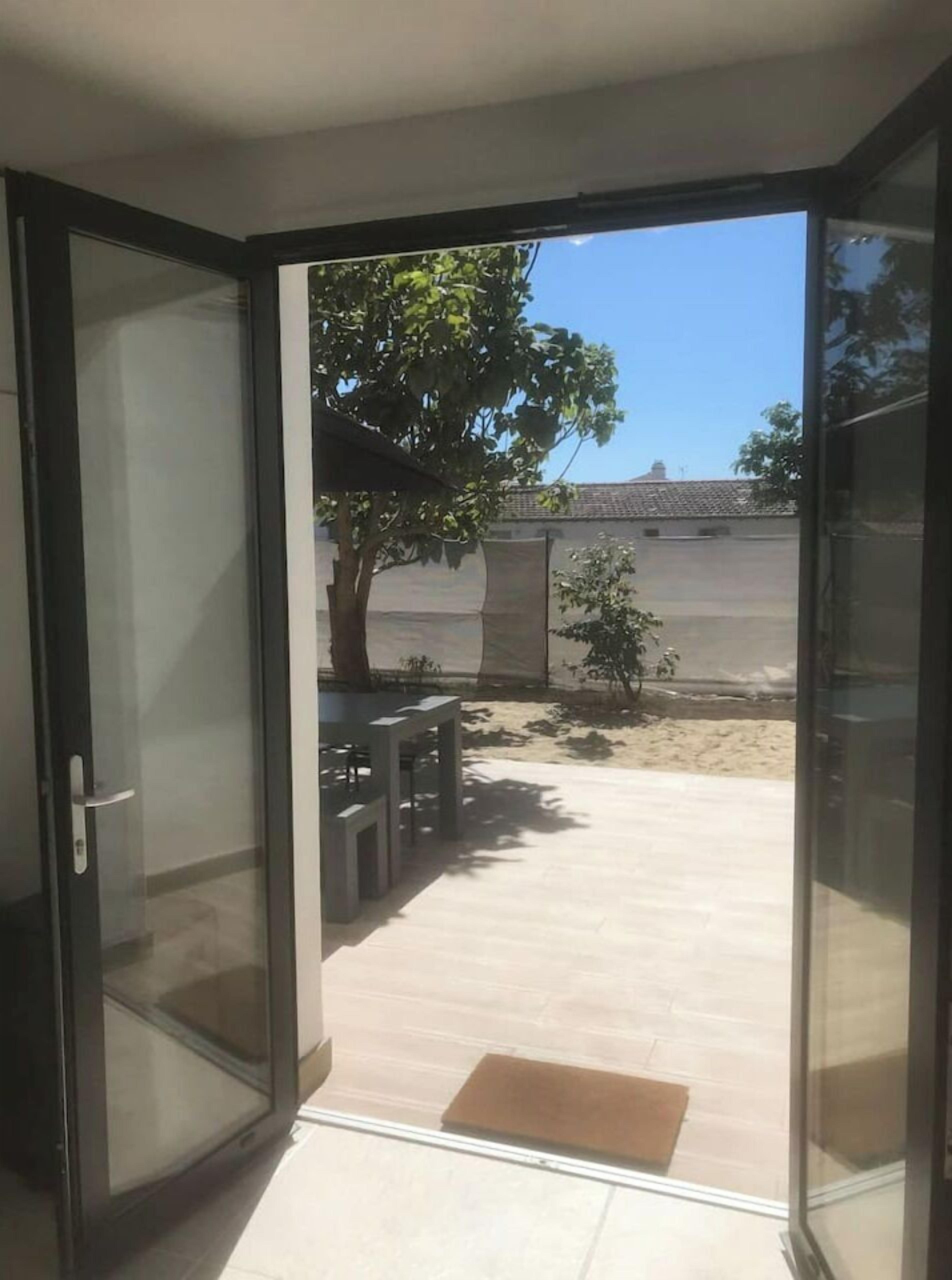 Une porte vitrée donne sur un patio doté d’un sol carrelé, d’une petite table et d’un arbre.