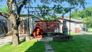 Zona exterior rústica amb una caseta de gos de fusta, una banca de pedra i un edifici de maó amb teulada vermella.