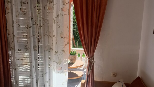 Un dormitori amb un llit, una finestra amb cortines lleugeres, vista a l'exterior i una planta en maceta a la finestra.