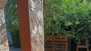 Zona de pati amb un pilar de pedra, una cadira de fusta i una taula amb una cistella de vimet.