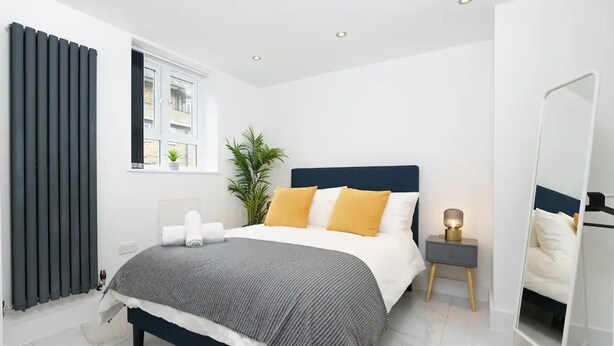 Quarto moderno com cama, mesa de cabeceira, abajur e janela com cortinas.