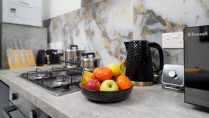 Cozinha com painel de parede de mármore, fogão a gás, chaleira, máquina de café e uma tigela de frutas.