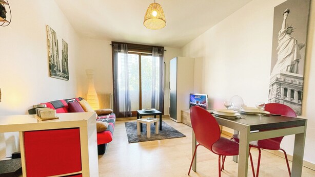 Un salon moderne avec un canapé, une table à manger et des chaises. On y trouve également un téléviseur, une lampe et un tableau accroché au mur.