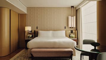 A hotel room with a large bed, a round glass table, a chair, a nightstand with a lamp, and a wall-mounted light fixture.