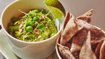 A bowl of guacamole with green peas and a lime wedge, accompanied by tortilla chips.