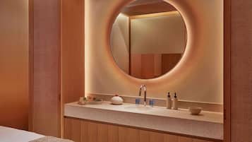 A modern bathroom with a round mirror, wooden paneling, and a vanity with toiletries.