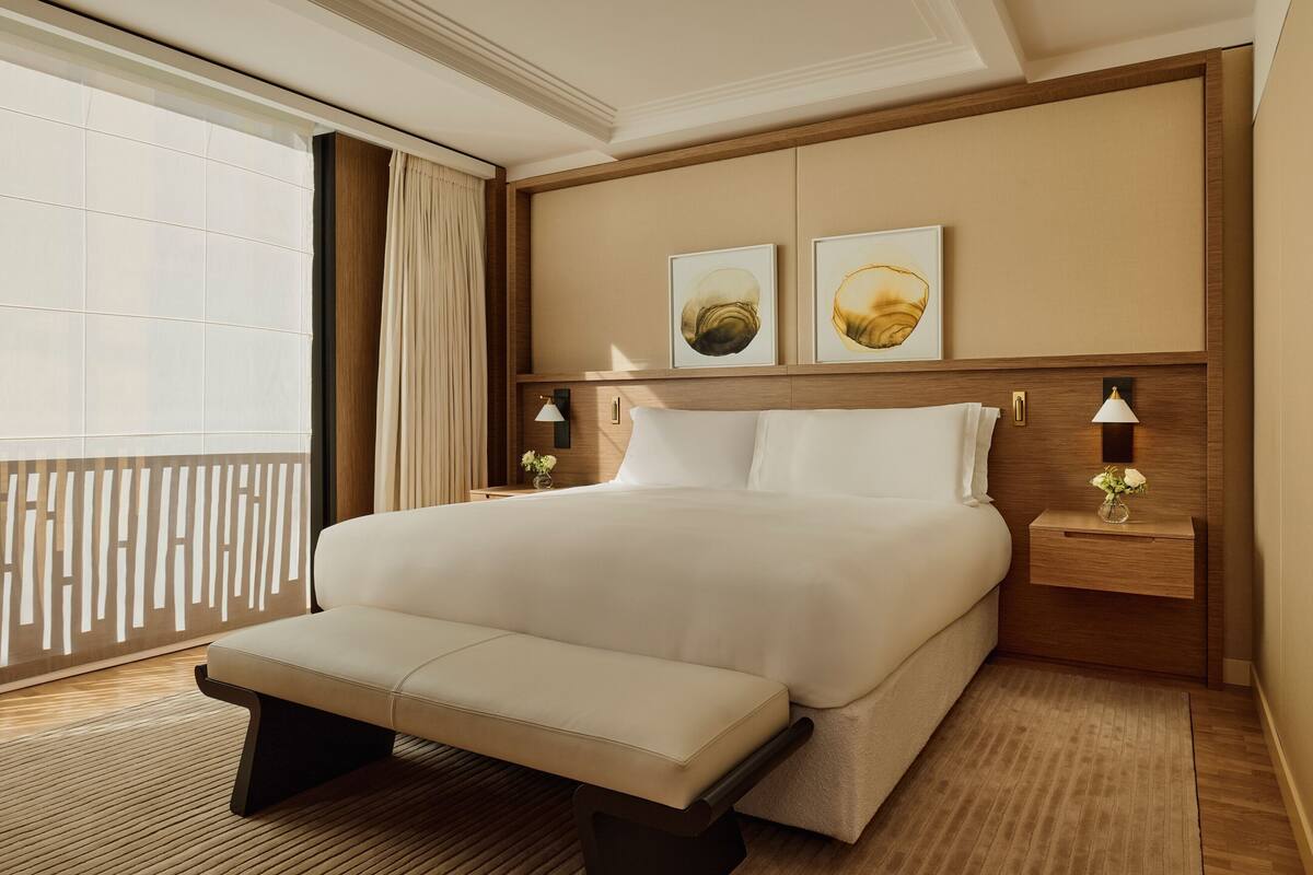 A hotel room with a large bed, a bench, two bedside tables with lamps, and artwork on the wall.