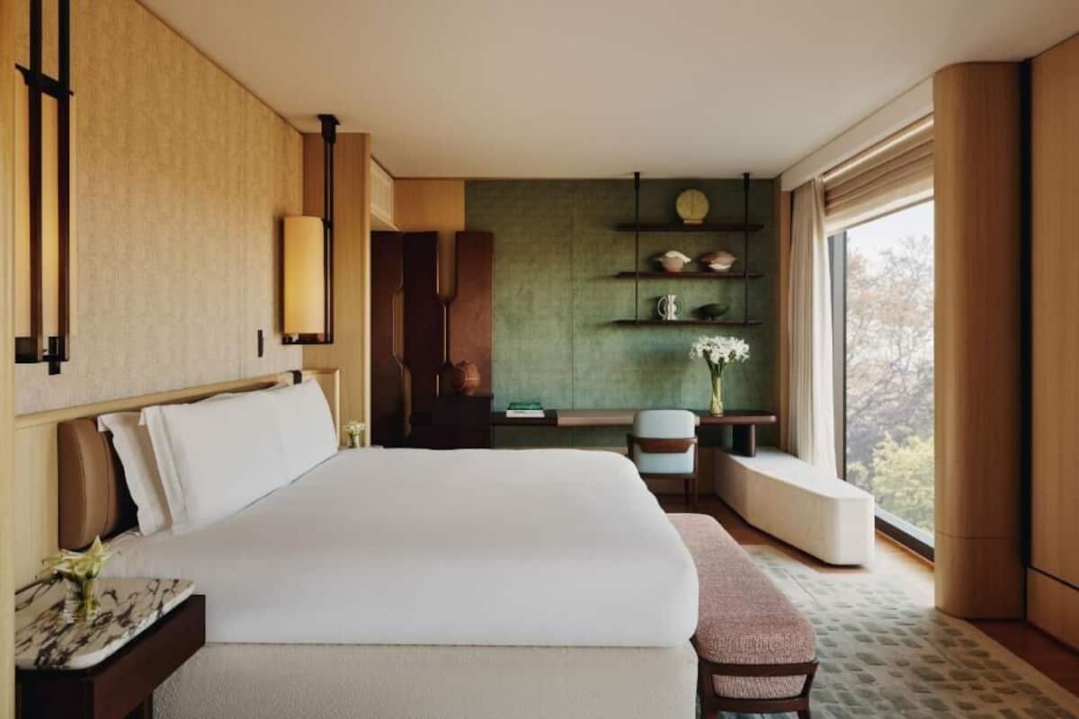 A modern hotel room with a large bed, a desk, a chair, and a view of the outdoors.
