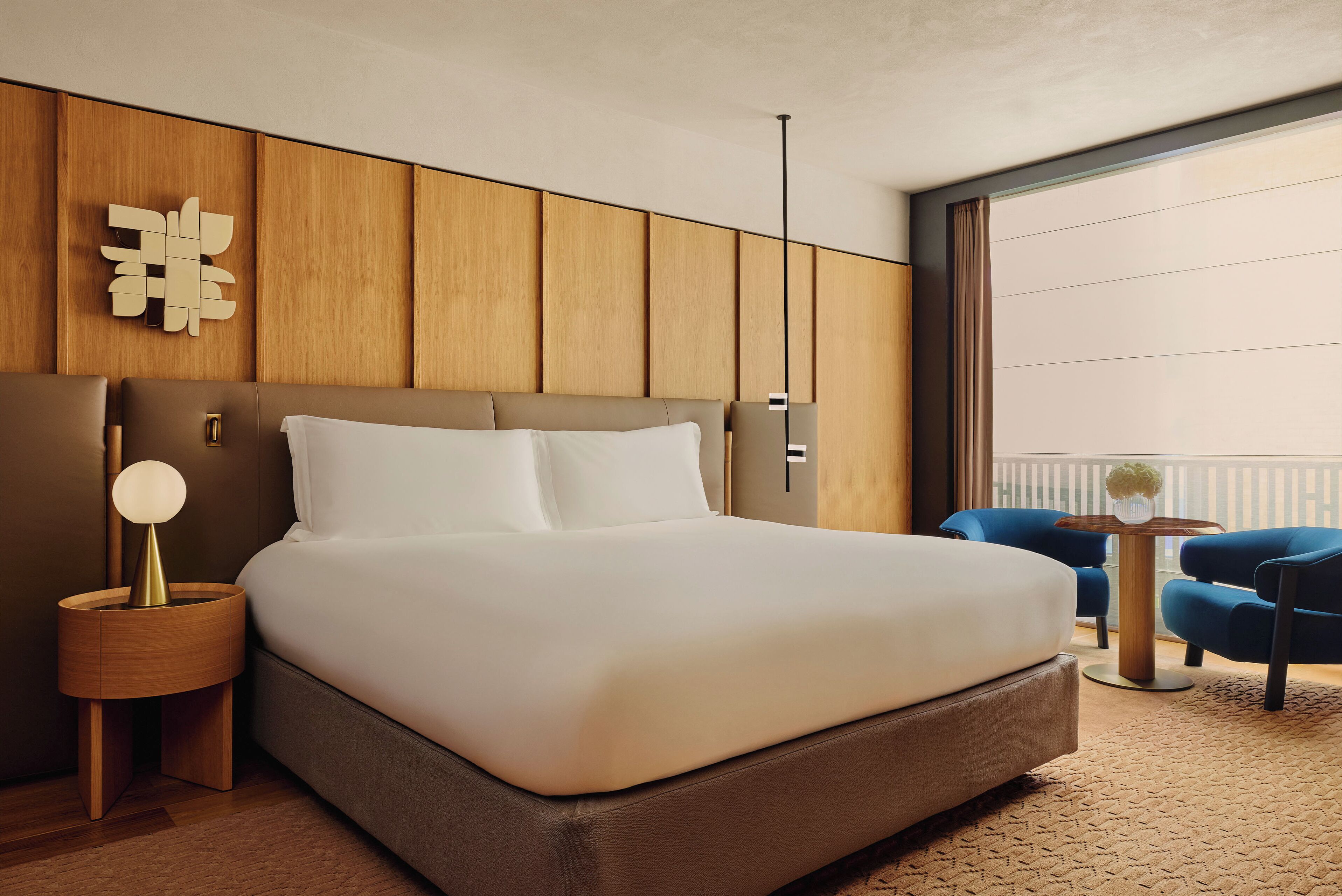 Een moderne hotelkamer met een groot bed, een houten hoofdbord, een nachtkastje met een lamp en uitzicht op het balkon.