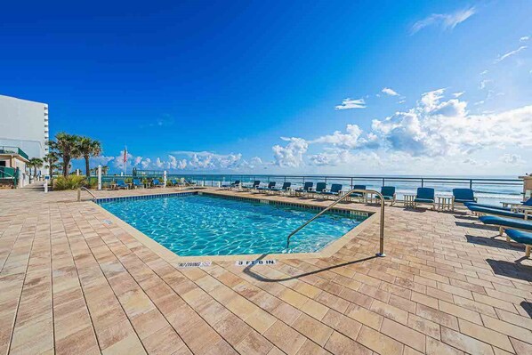 A pool area with a clear view of the ocean, a flag, and a sign indicating the pool depth.