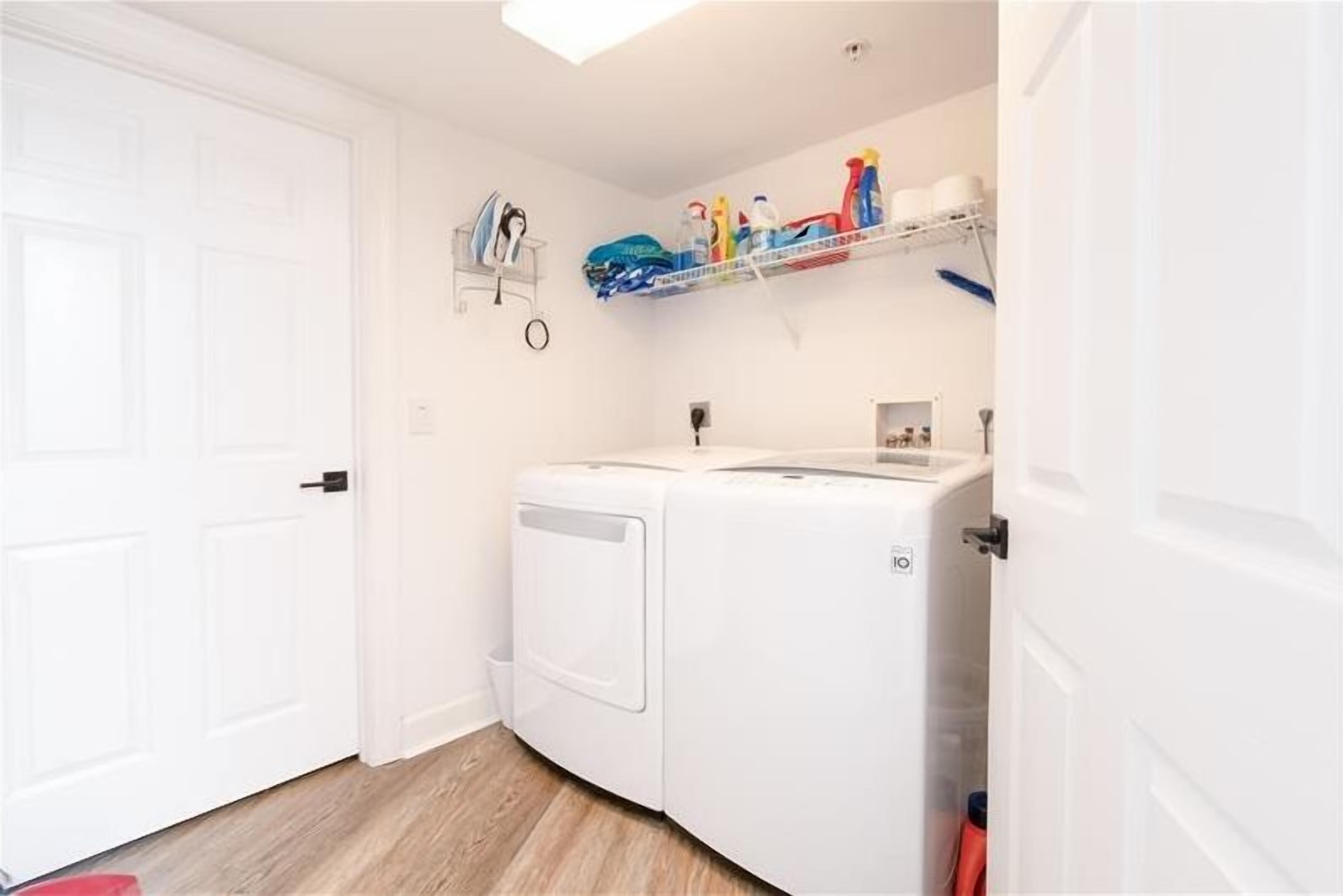 A laundry room with a washing machine, a drying rack, and shelves with cleaning supplies.