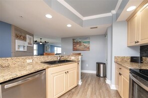 A kitchen with granite countertops, a dishwasher, a sink, wooden cabinets, and a painting on the wall.