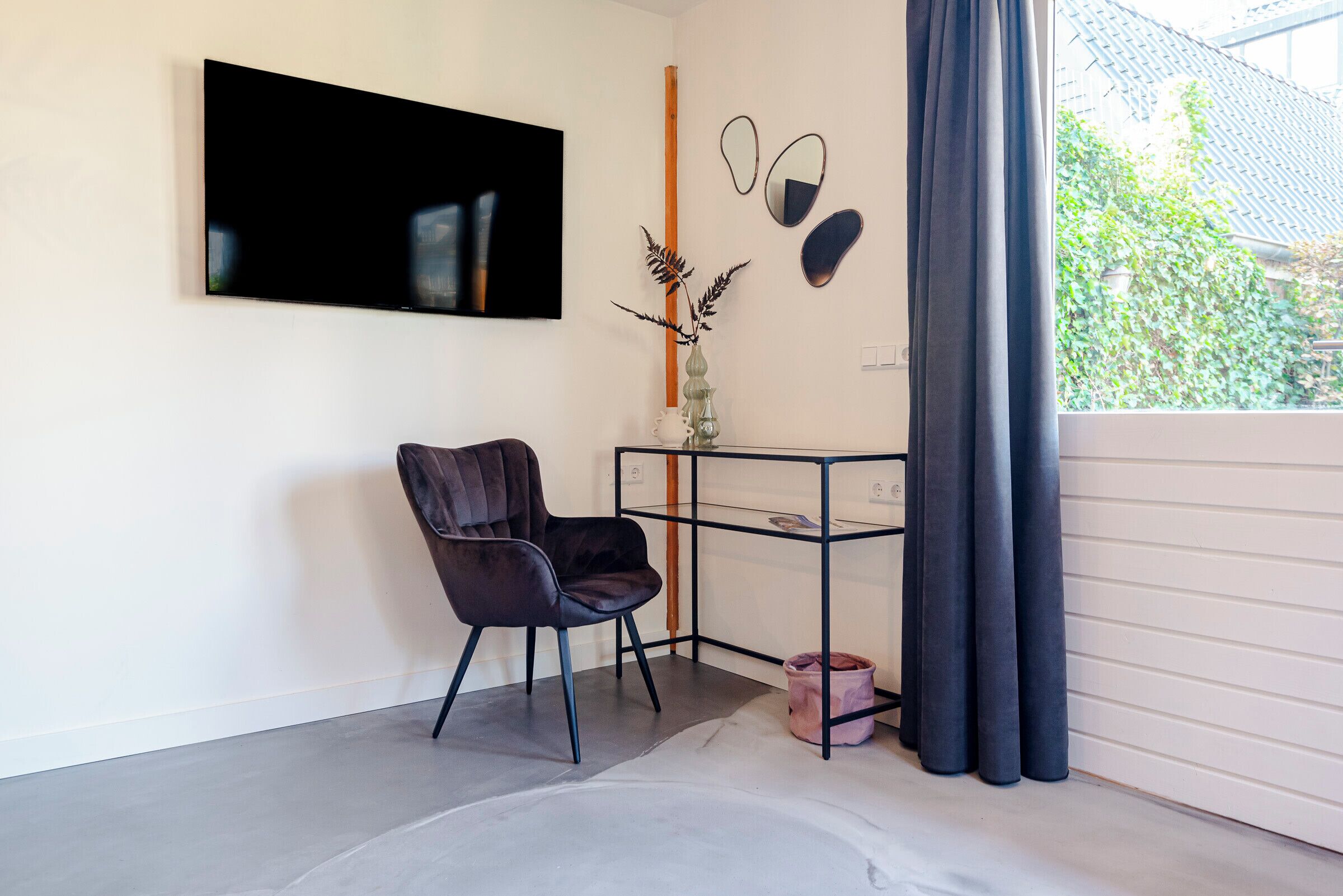 Una habitación moderna con una butaca de cuero negro, una mesita de cristal y un televisor montado.