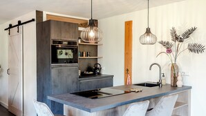 Una cocina moderna con una isla central, taburetes de bar, iluminación colgante y una pared de acento de madera.