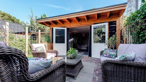 Un patio al aire libre con mobiliario de mimbre, una pérgola de madera y vistas de la casa.