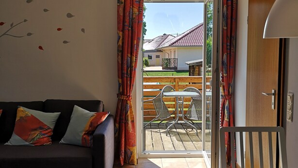 A living room with a sofa, a table, and a view of an outdoor patio with chairs and a table. - Vacation apartment Hermann (Bovenden)