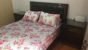 Un letto con biancheria da letto floreale, una testiera in legno, un comodino con una lampada e una presa di corrente.