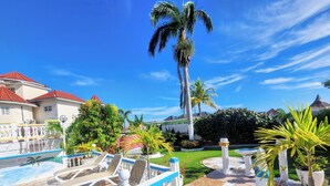 A pool area with lounge chairs, a palm tree, and a well-maintained lawn. - Pink Hibiscus Villa (Montego Bay)