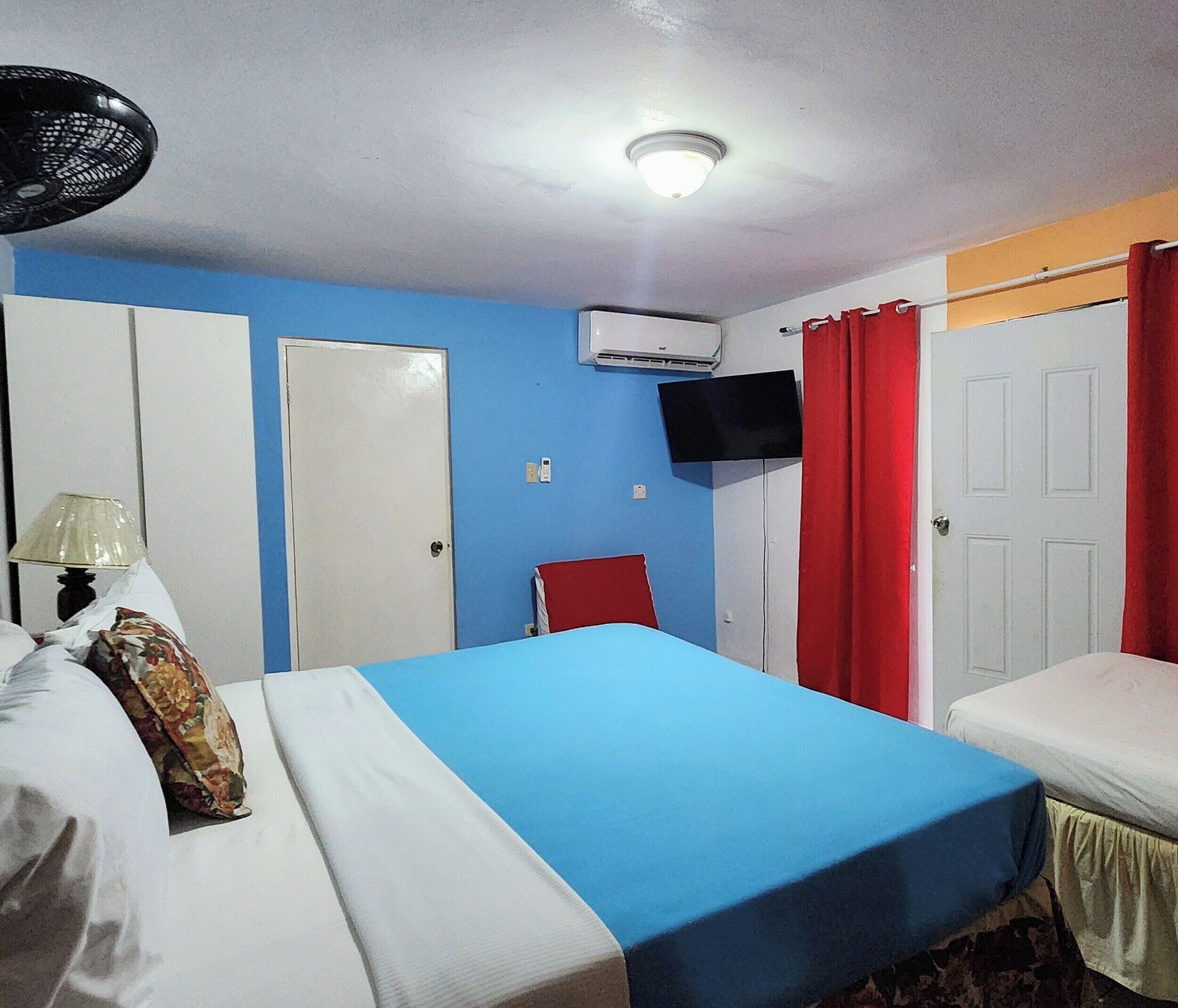A room with a bed, a bedside table with a lamp, a TV mounted on the wall, and an air conditioning unit.