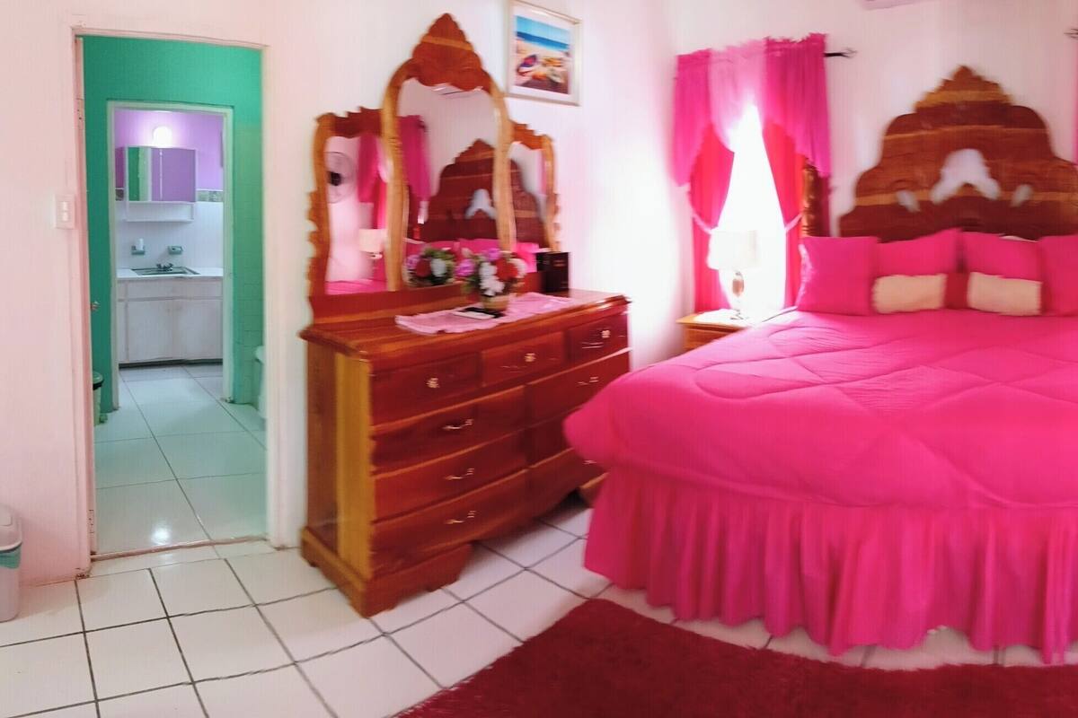 Un dormitorio con una cama grande, un aparador, un espejo y una puerta que da a un baño.