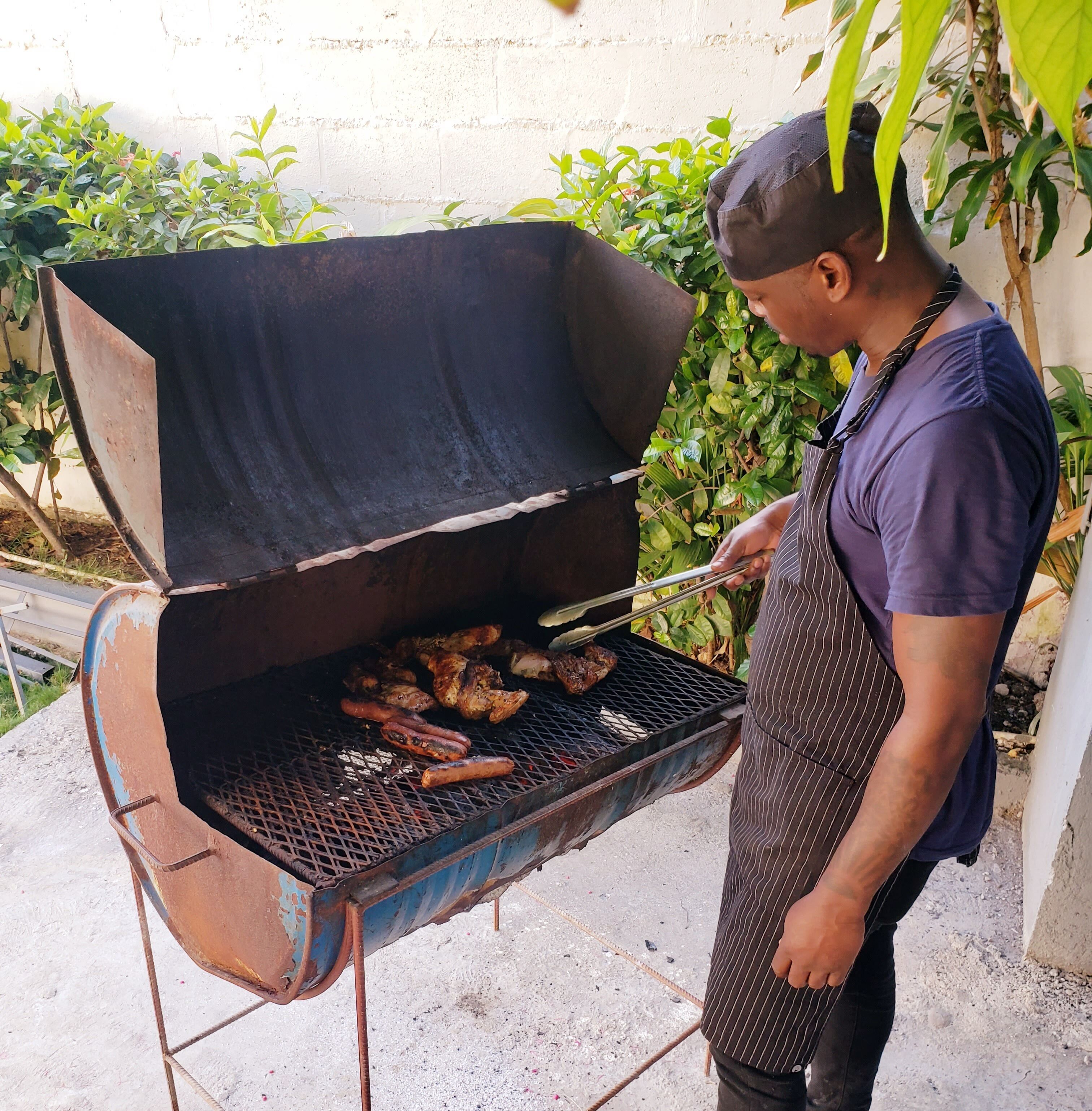 A man grilling food outdoors on a makeshift grill with a metal frame and a large open cooking area.