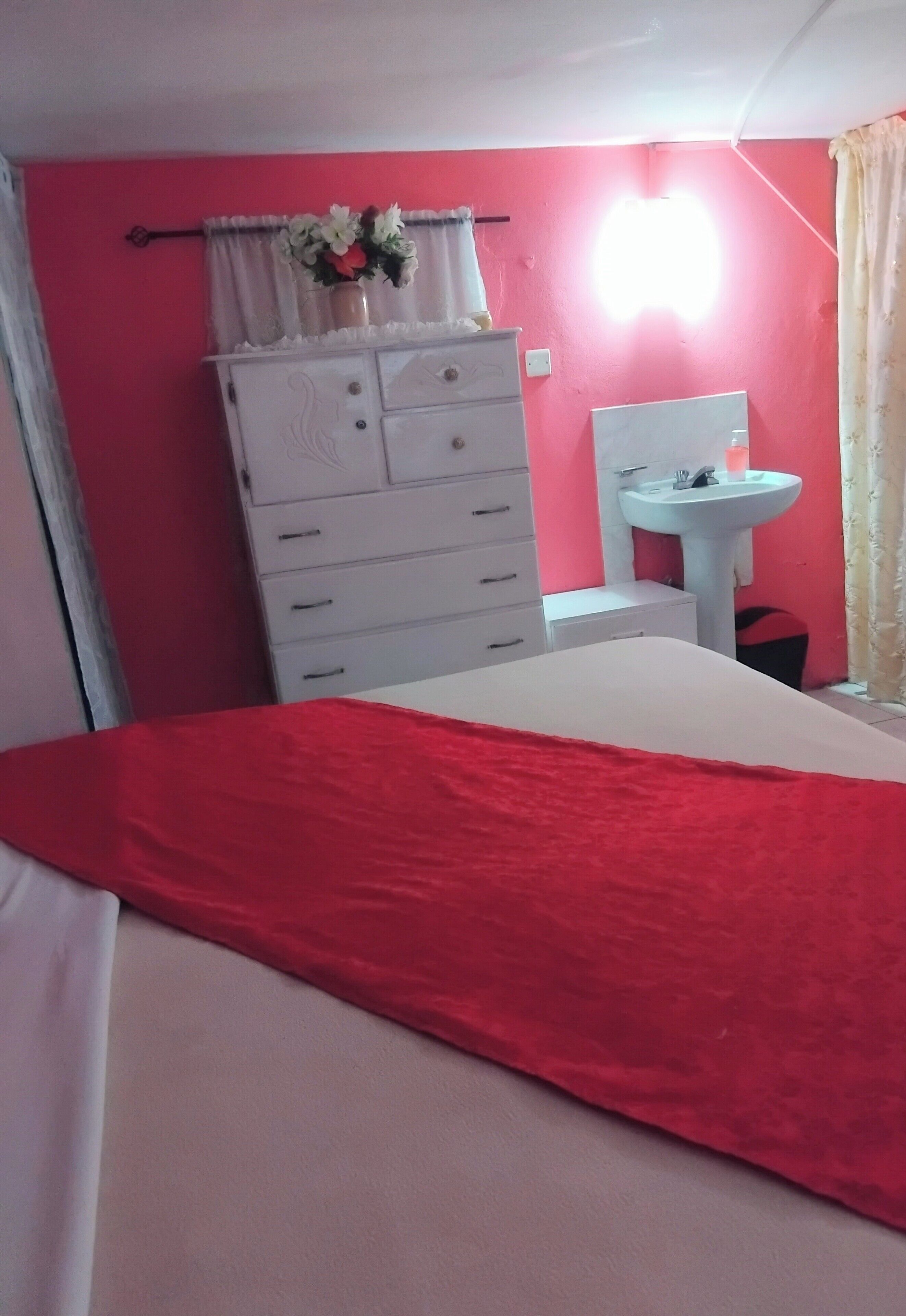 A bedroom with a bed, a dresser, a vanity, and a wall-mounted light.