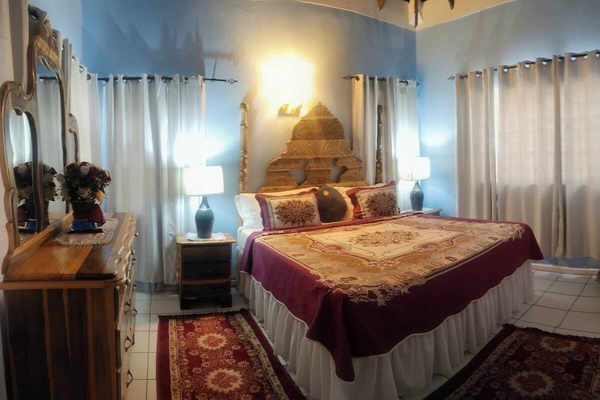 Un dormitorio con cama, mesita de noche, silla, cómoda y lámpara de pared.