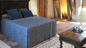 A bedroom with a large bed, wooden beams, a wooden door, and a small table with a vase. - Les Trois-Moutiers (Les-Trois-Moutiers)