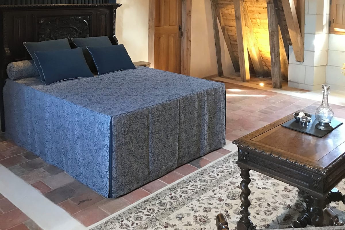 A bedroom with a large bed, wooden beams, a wooden door, and a small table with a vase.