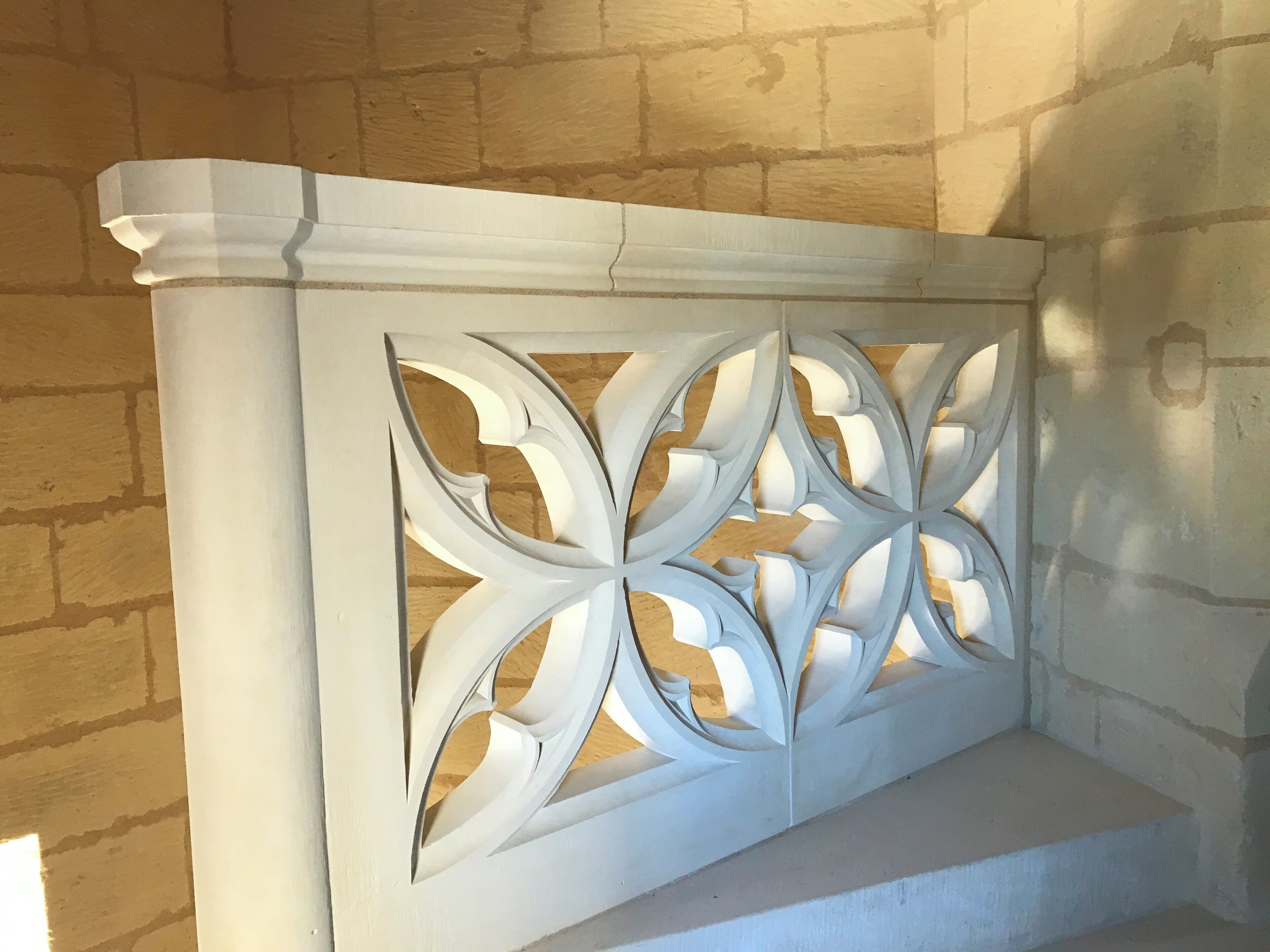 Ein weißes, dekoratives Wandpanel mit geometrischem Muster, an einer Ziegelwand befestigt.