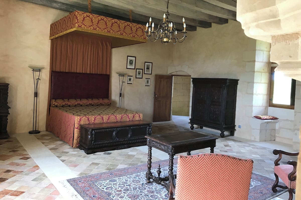 A bedroom with a four-poster bed, a chandelier, a wooden cabinet, and a patterned rug.
