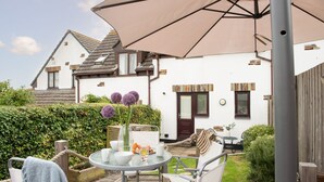 A patio with a round table, chairs, and a large umbrella. - Sunshine Cottage -  a cottage that sleeps 4 guests  in 2 bedrooms (Padstow)