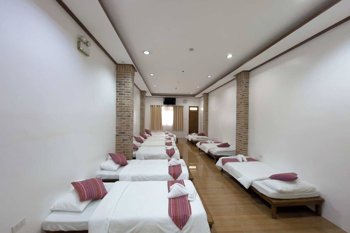 A hotel room with multiple beds aligned in a row, each with white bedding and red pillows.