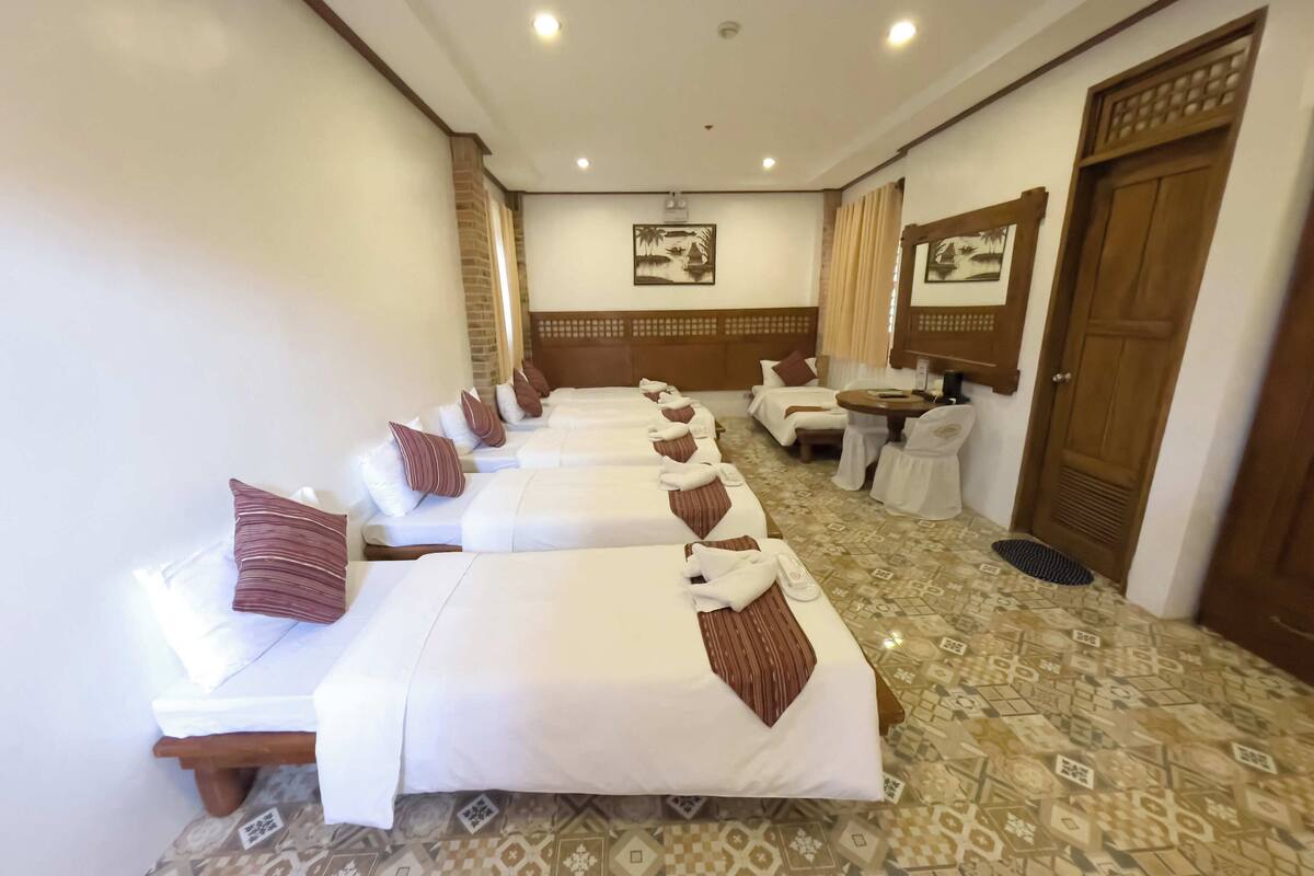 A hotel room with four single beds, a small table, and a chair.