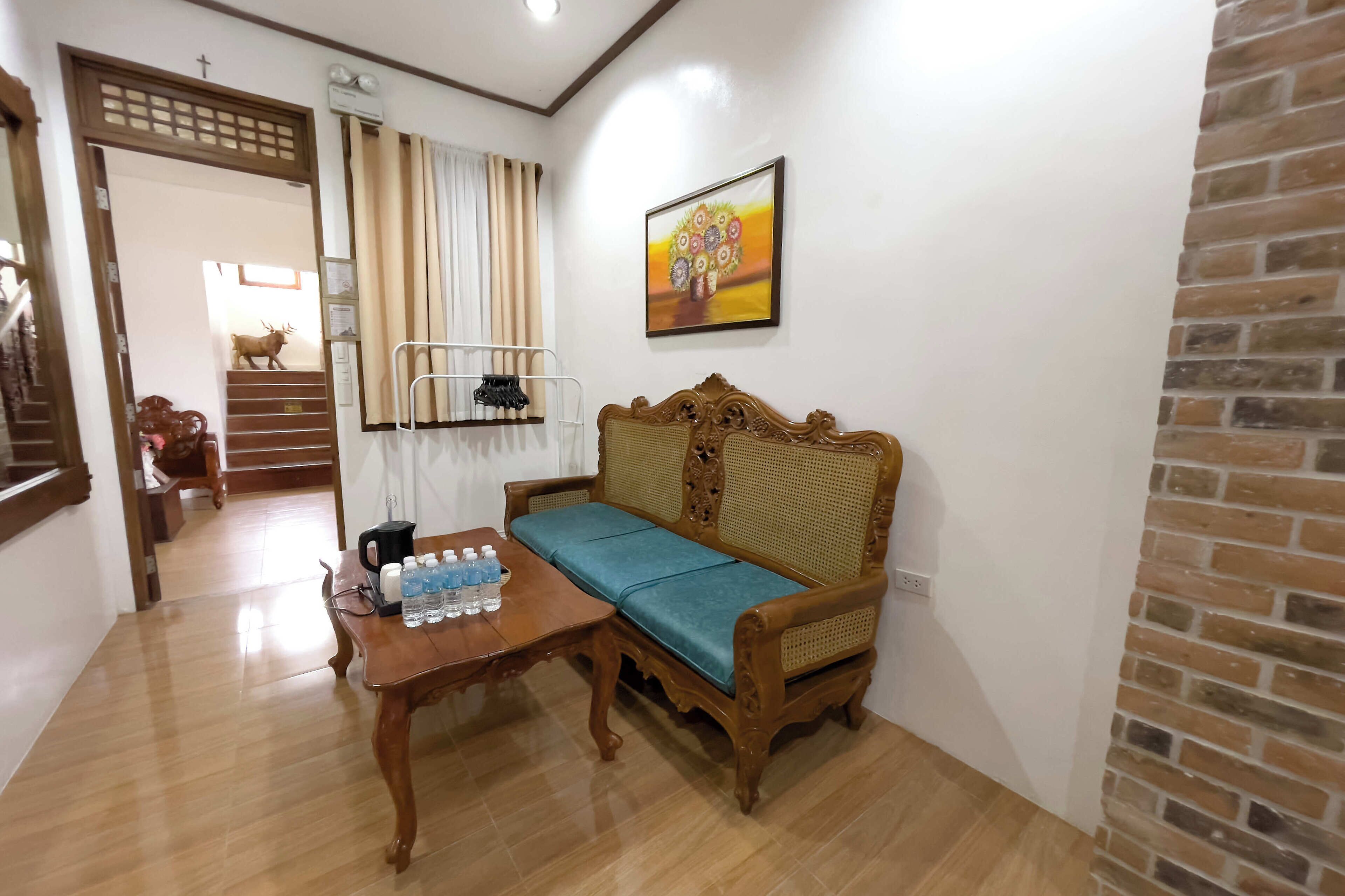 Una habitación con un sofá de madera, una mesa con botellas de agua, una escalera y un cuadro colgado en la pared.