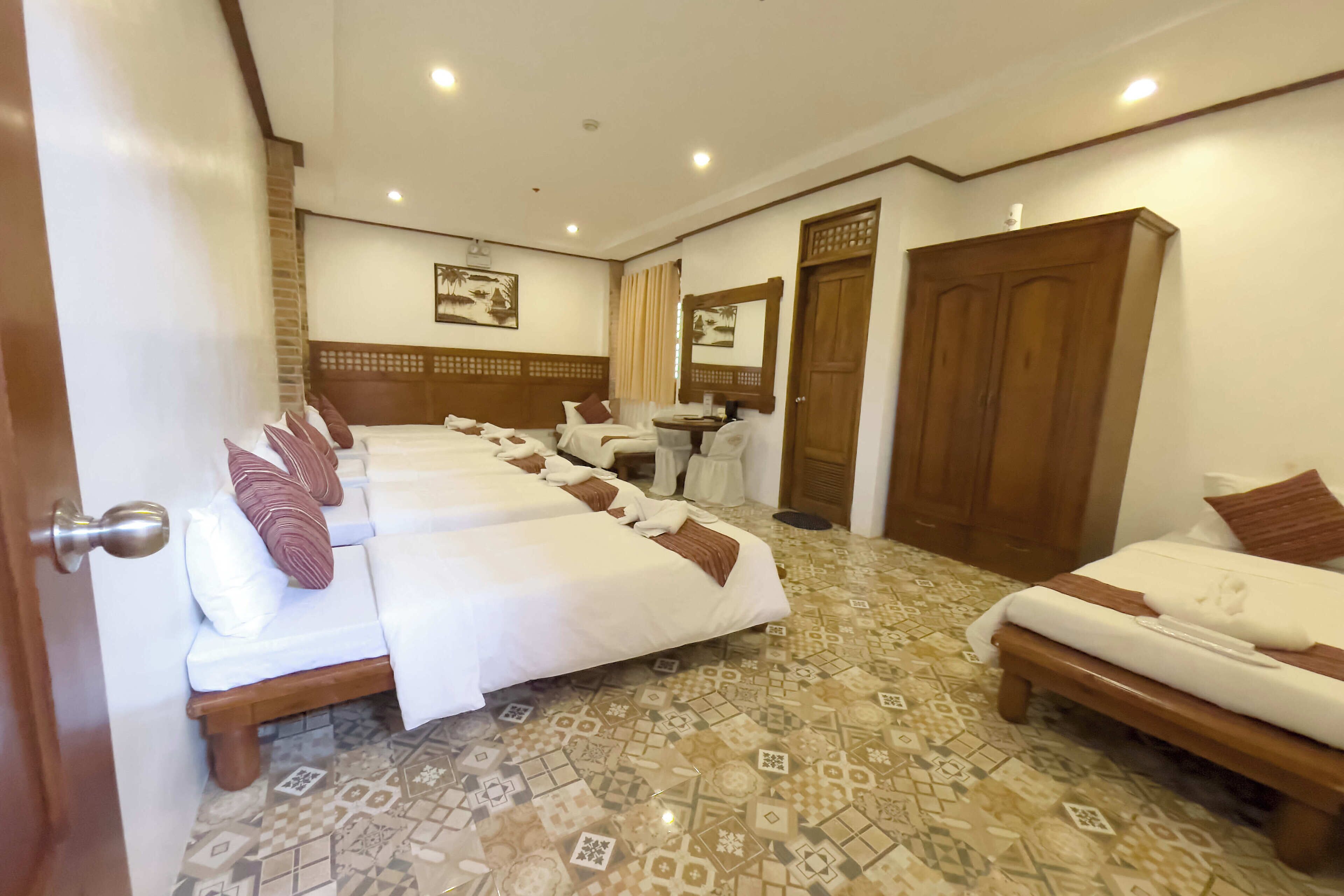 A hotel room with two beds, a wooden wardrobe, a bathroom with a mirror, and patterned floor tiles.