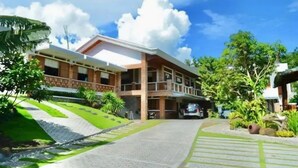 A two-story building with a balcony, surrounded by greenery and a paved driveway. - Casa Lorenzo powered by Cocotel (Daraga)