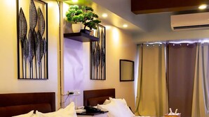 A hotel room with two beds, a nightstand, a potted plant, and artwork on the walls. - Deluxe Family Room in Tagaytay With Taal Lake View (Tagaytay)