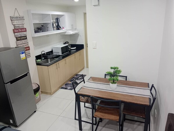 Una cocina compacta equipada con refrigerador, microondas e instalación de lavavajillas. Hay una mesa de comedor con sillas y una pequeña planta en maceta.