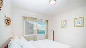 Une chambre à coucher avec un lit, une fenêtre donnant sur la mer et deux tableaux encadrés accrochés au mur.