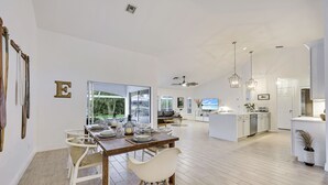 Ein geräumiger Wohnbereich mit Esstisch für sechs Personen, einer Küche und einem großen Fenster mit Blick ins Freie.