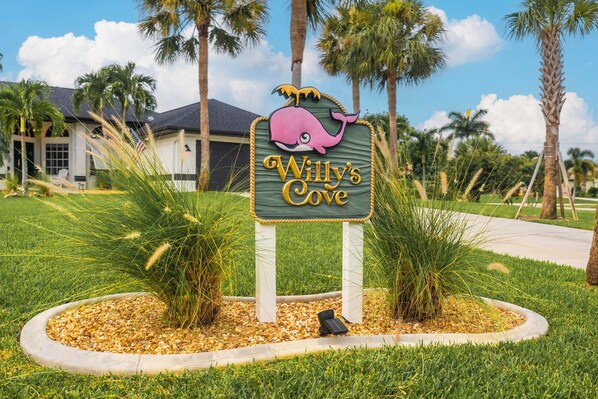 A sign for "Willy's Cove" with a whale graphic, surrounded by palm trees and grass.