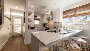 A modern kitchen with white cabinetry, a large island with stools, and a view of the outdoors through the windows. - Sandestin, Baytowne Wharf, Golf Cart, Pool (Miramar Beach)