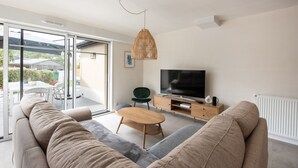 A modern living room with a sofa, a coffee table, a TV, and a dining area with chairs and a table. - Seaside house, all comforts - close to the beaches (Dinard)